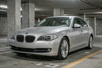 BMW Série 5 F10 grise garée dans un parking souterrain urbain, défauts visibles sur la carrosserie et traces de rouille autour des passages de roue