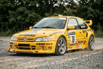 Peugeot 306 Maxi jaune vue de trois quarts avant sur zone de service en gravier, carrosserie élargie et décalcomanies sponsors